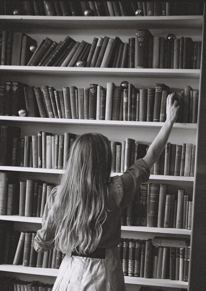 Black and white shot of a girl reaching for a book in a library featured on TheNuminous.net